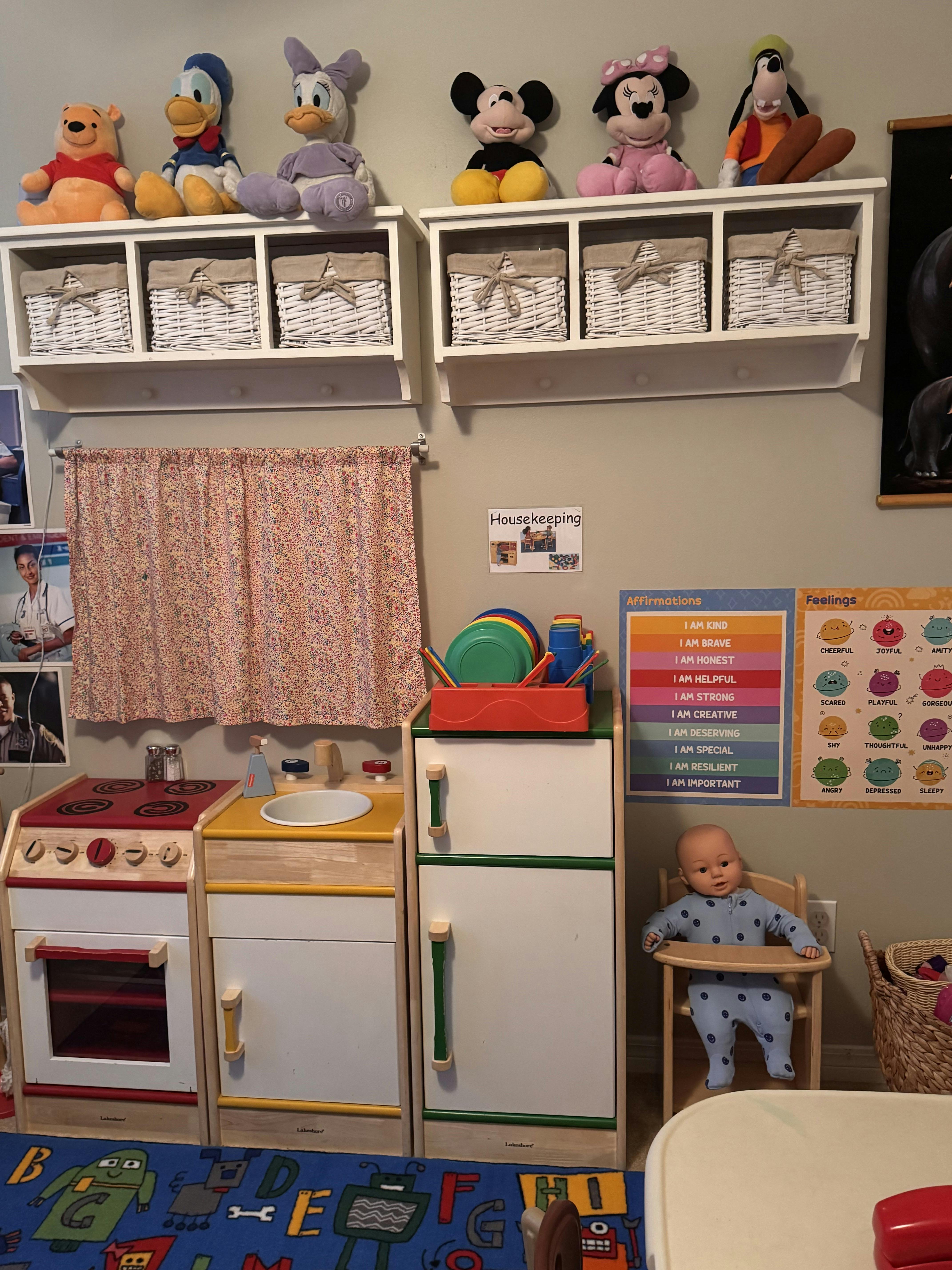 Play kitchen area with a doll in a high chair and shelves of stuffed toys