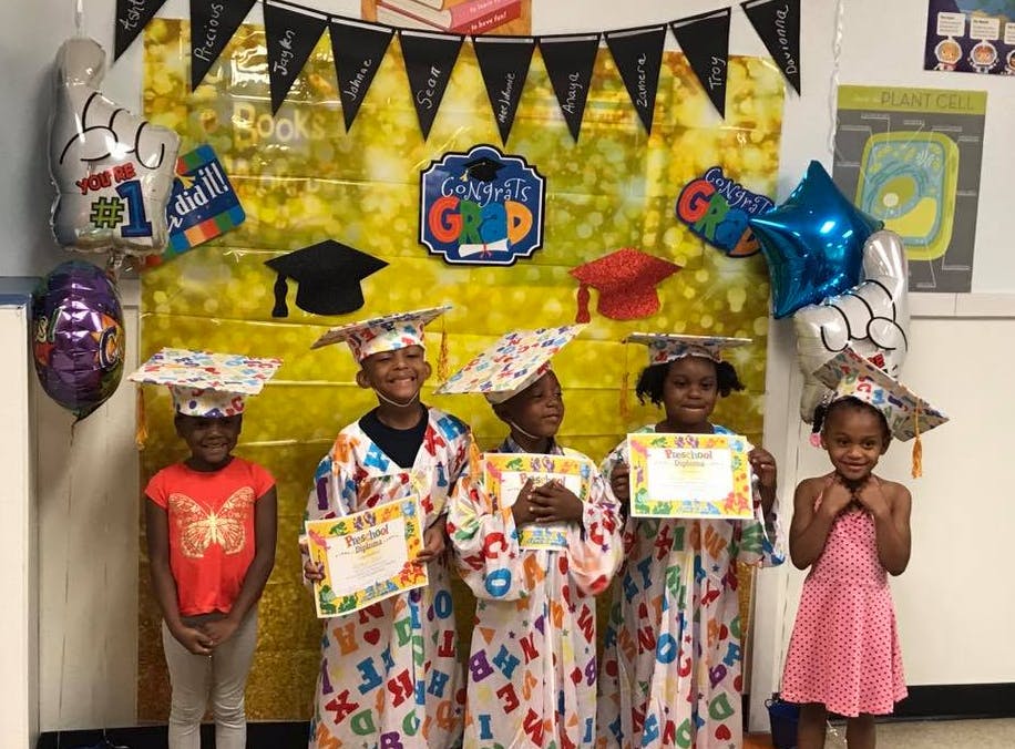 Five children in graduation caps and gowns holding certificates