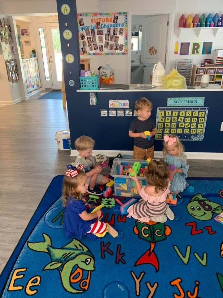 Children playing with toys on a blue alphabet rug in a classroom