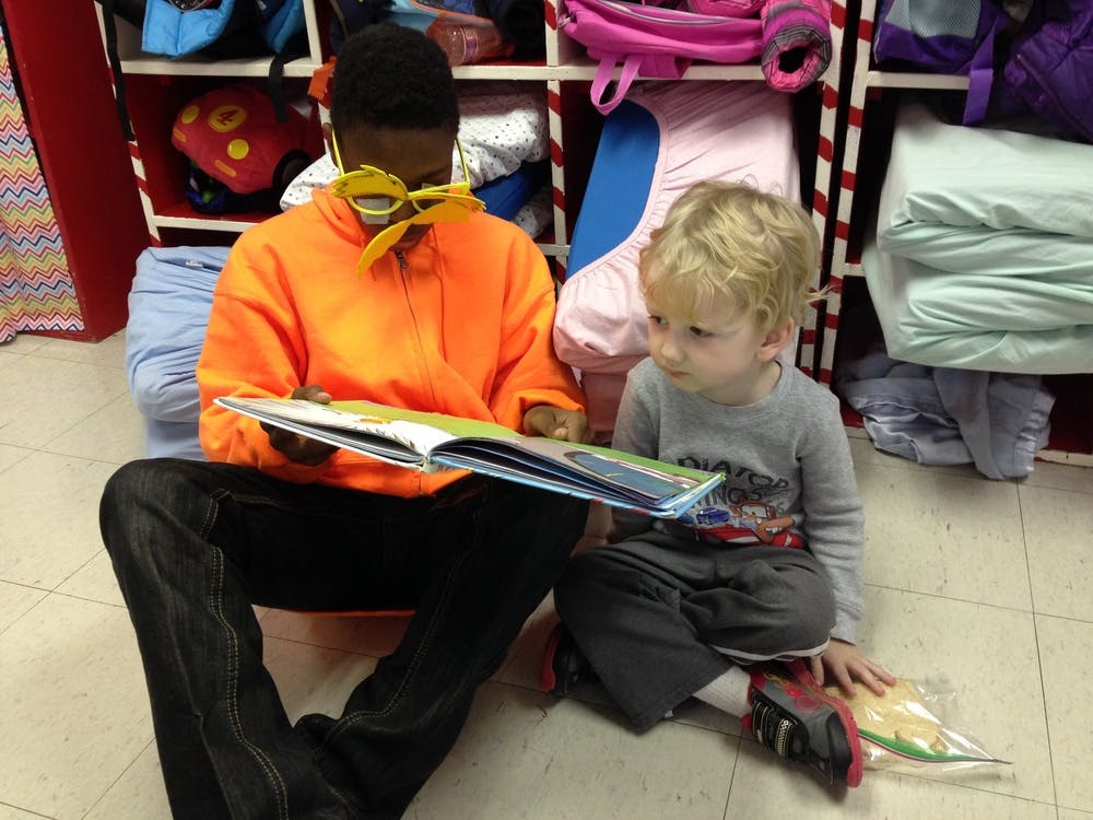 Person and child sitting on floor reading a book together