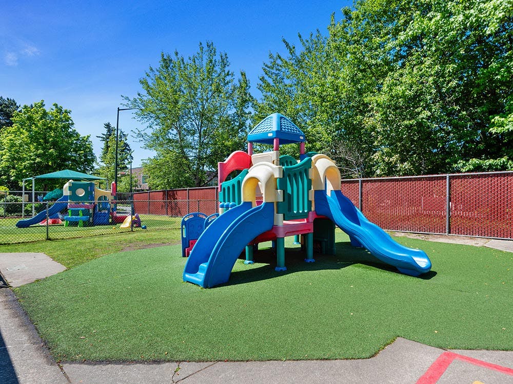A colorful playground with plastic slides and climbing structures on artificial turf