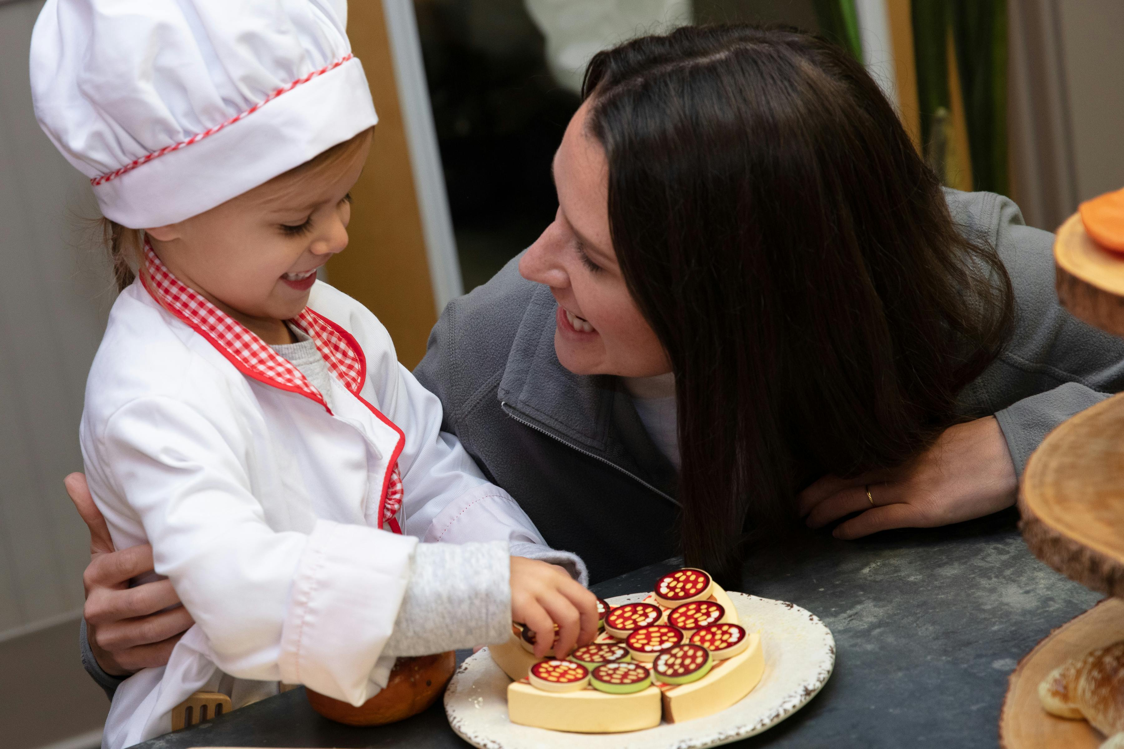 Person and child in chef's hat playing with toy food
