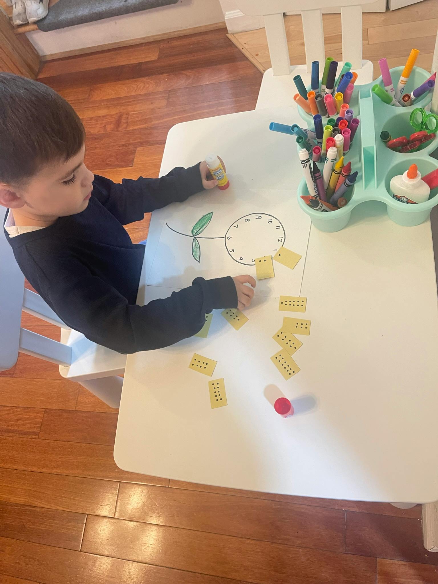 Child drawing on paper at a table with markers and small yellow cards