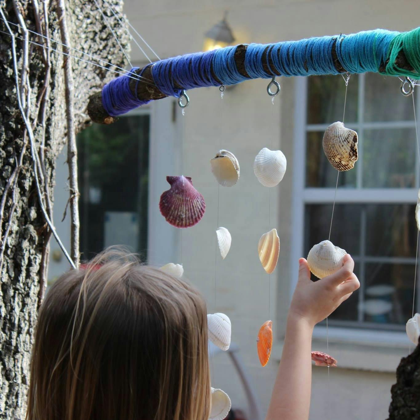Child reaching for a seashell hanging from a yarn-wrapped stick