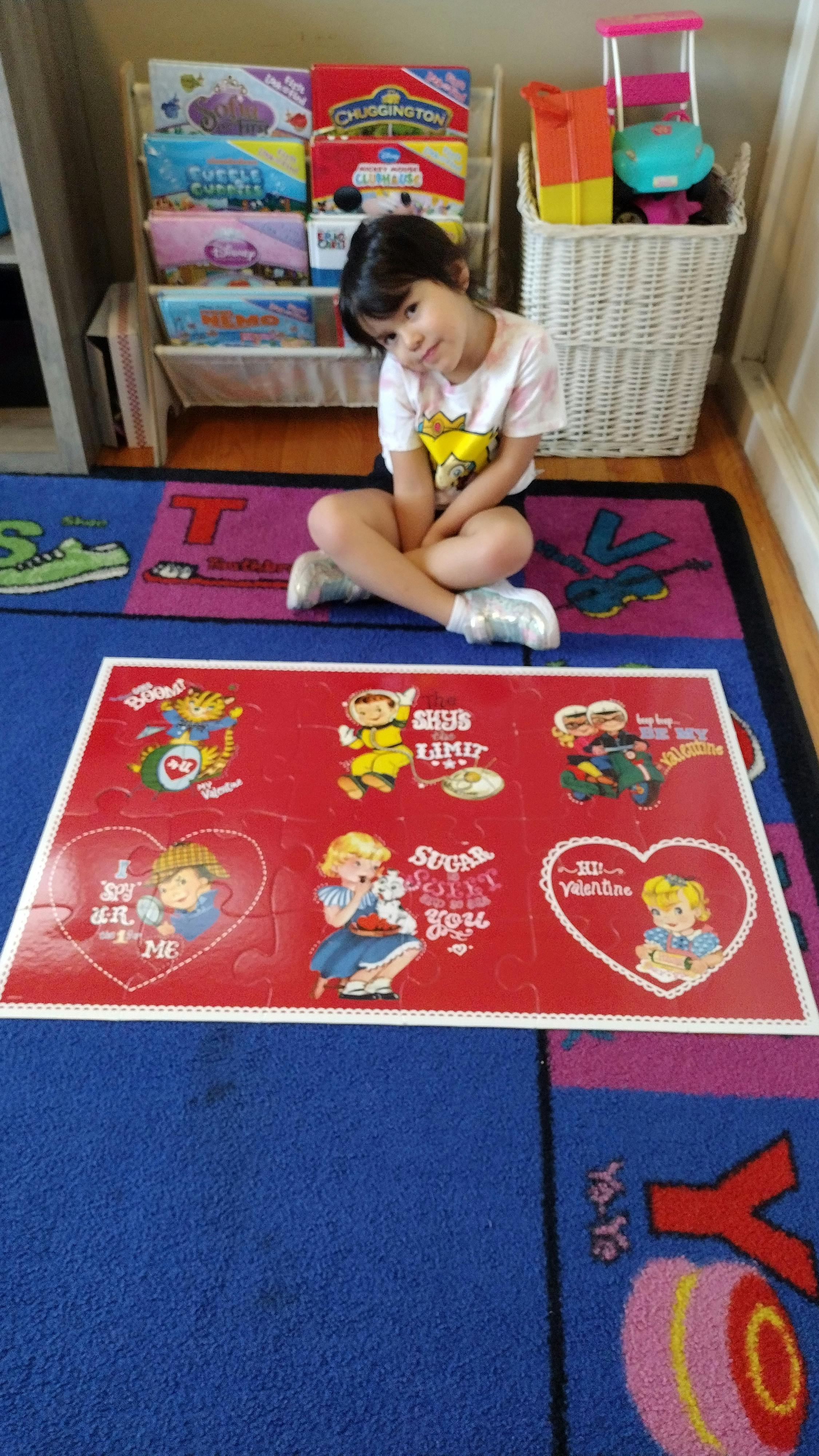 Child sitting on an alphabet rug next to a completed Valentine themed puzzle
