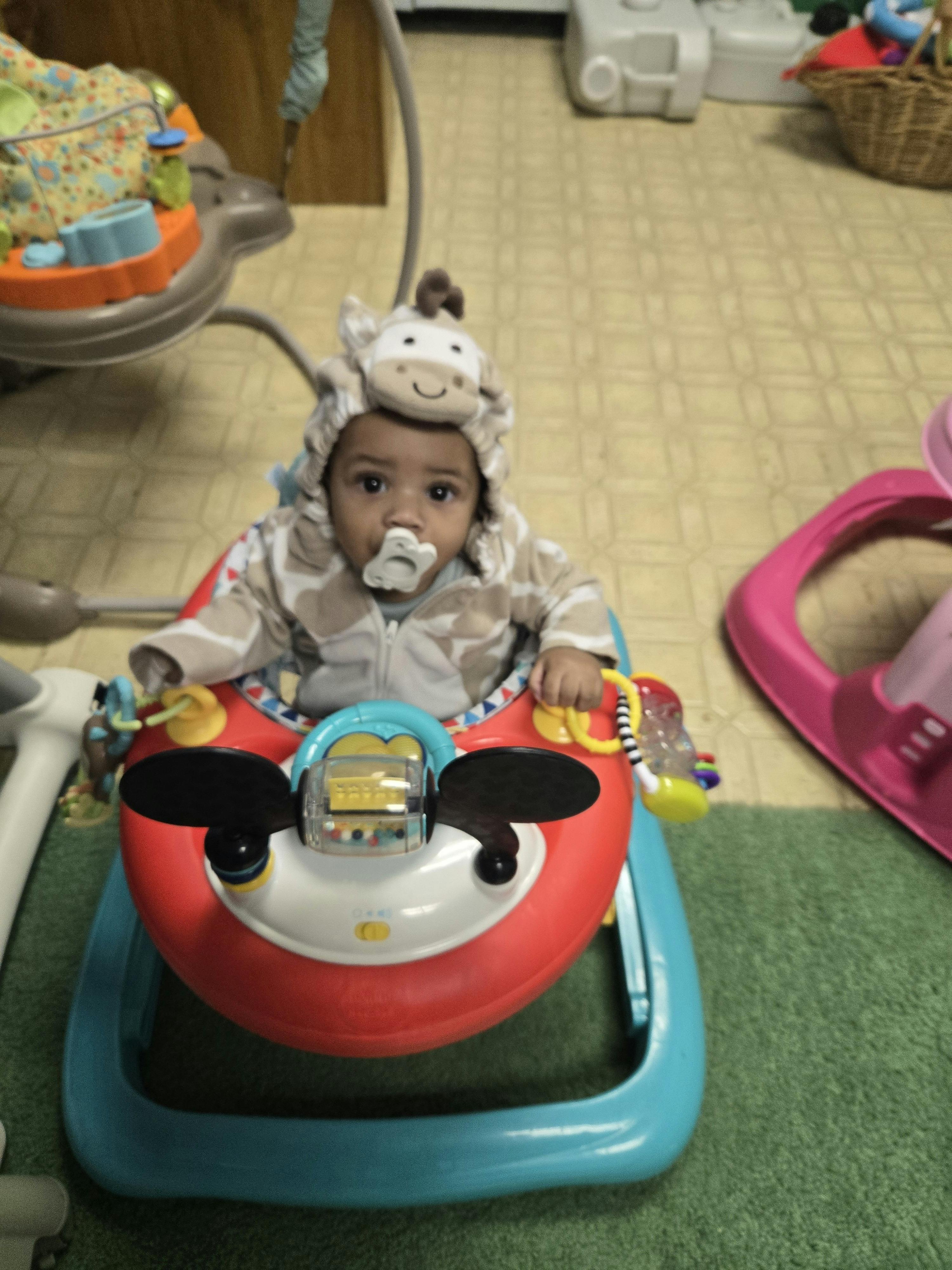 Child wearing an animal hood sitting in a toy activity walker
