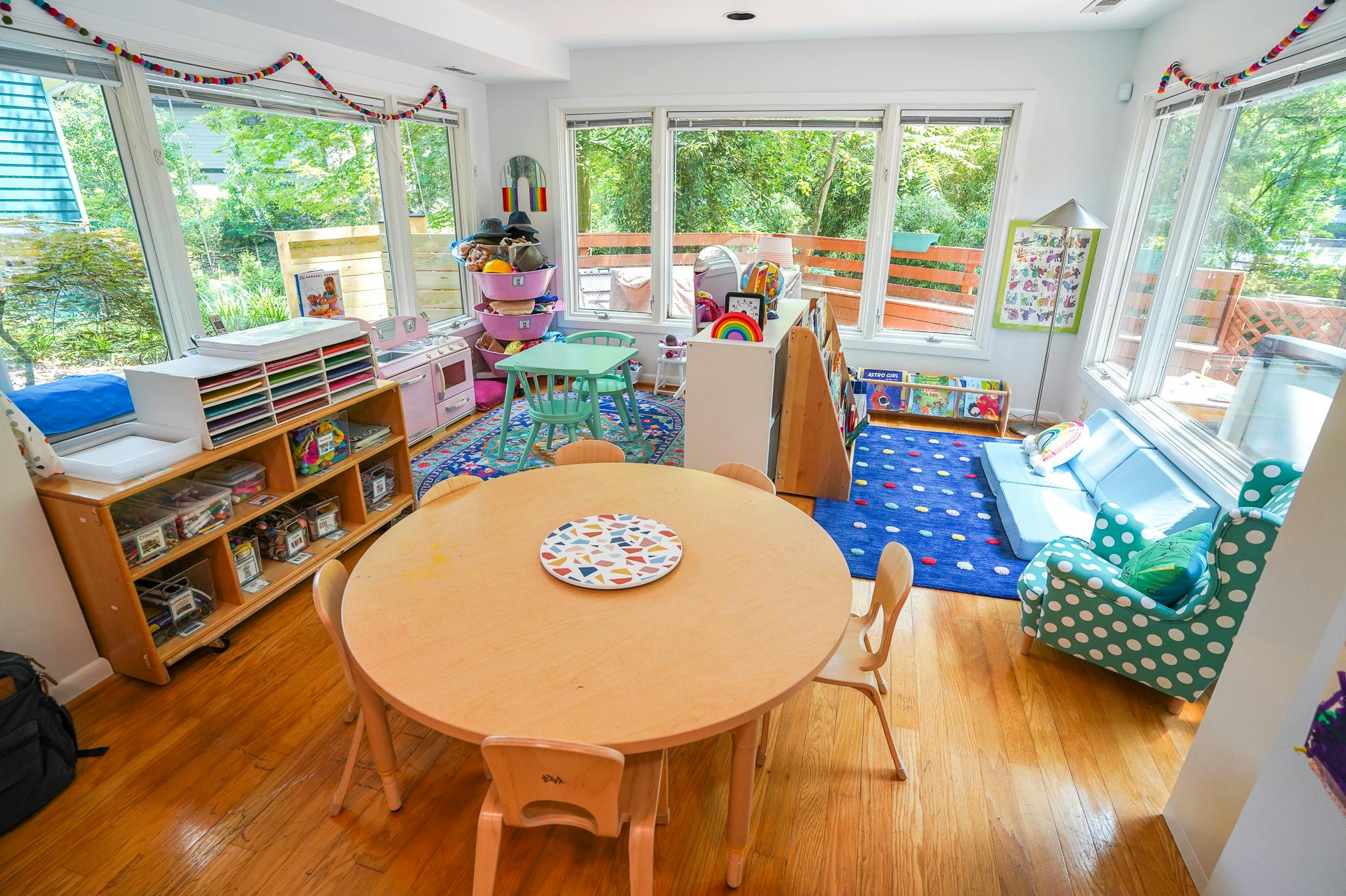A bright classroom with small tables and chairs, shelves, and large windows