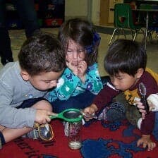 Three children looking at an object through a magnifying glass