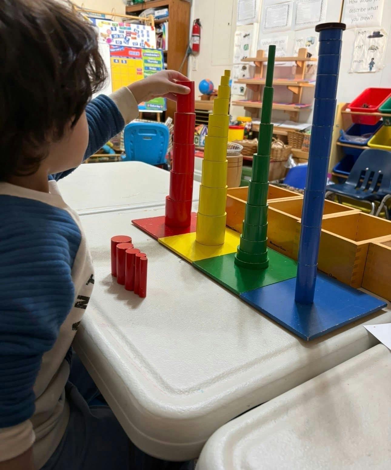 Child building a red tower with blocks on a table in a classroom