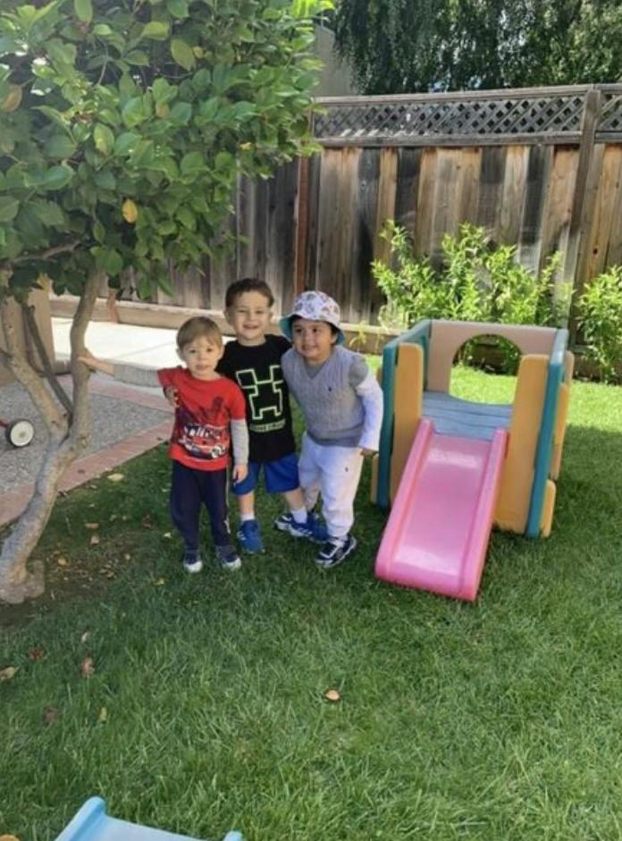 Three children standing together in a yard by a small slide