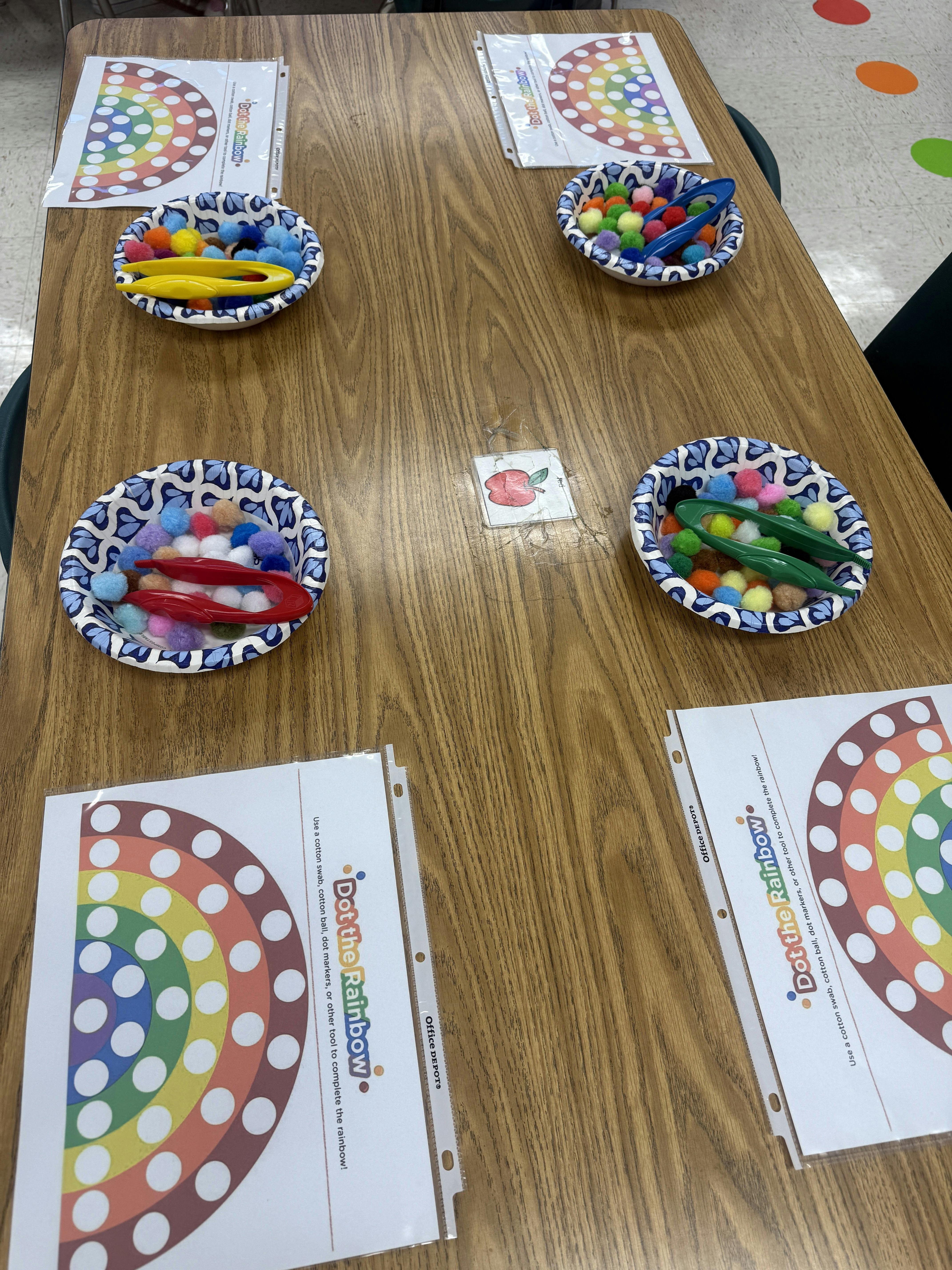 Dot the Rainbow activity sheets with bowls of pom-poms and tweezers on a table