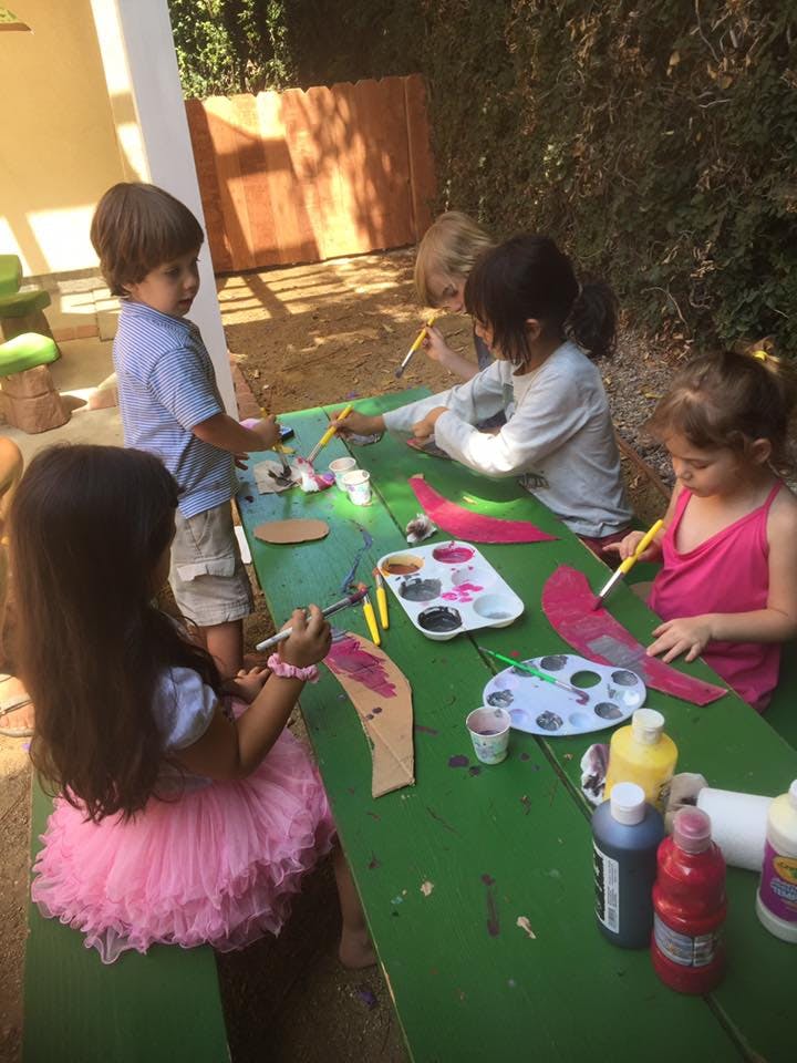 Children painting at a green table outdoors