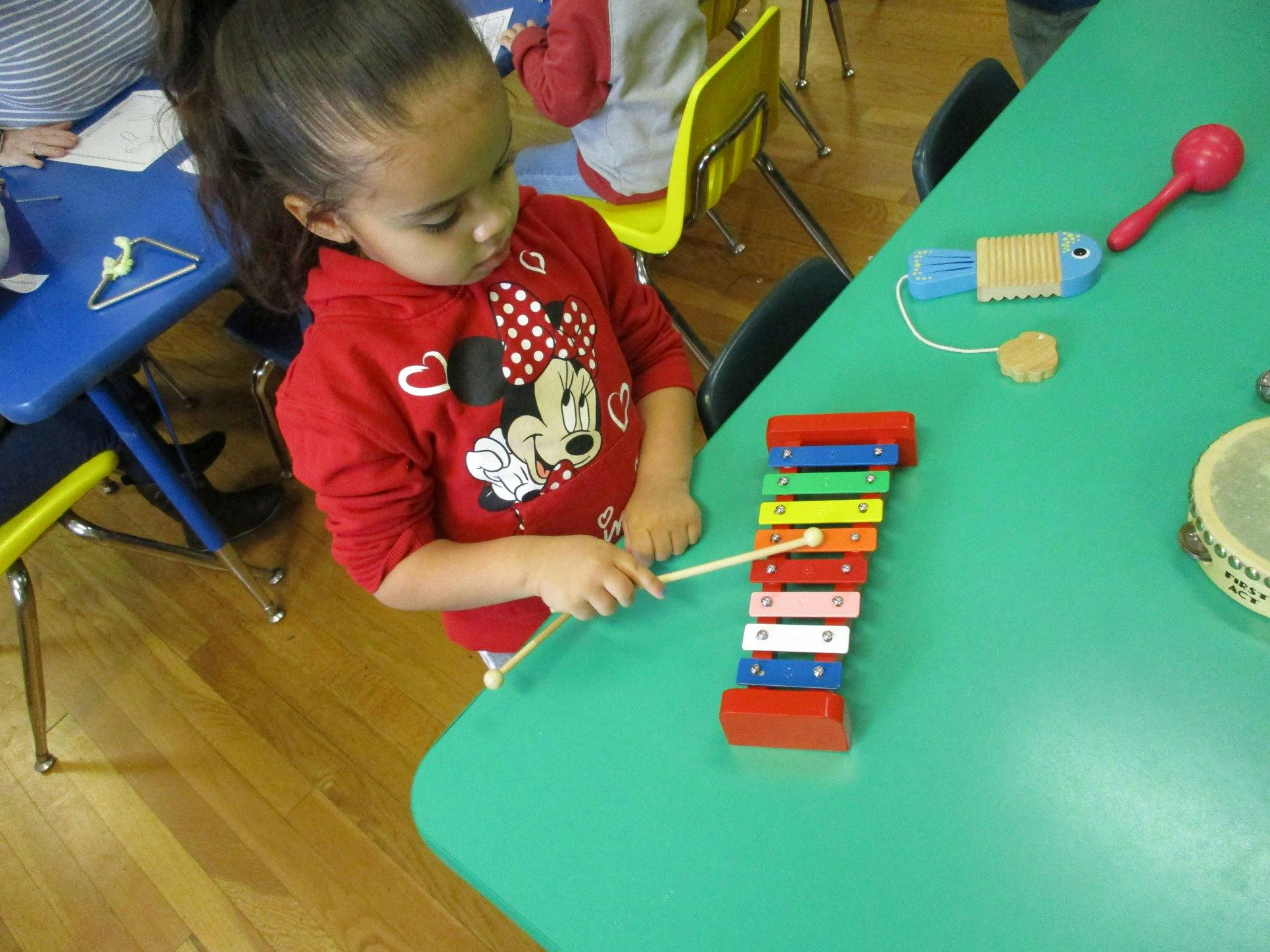 Child playing a colorful xylophone on a green table