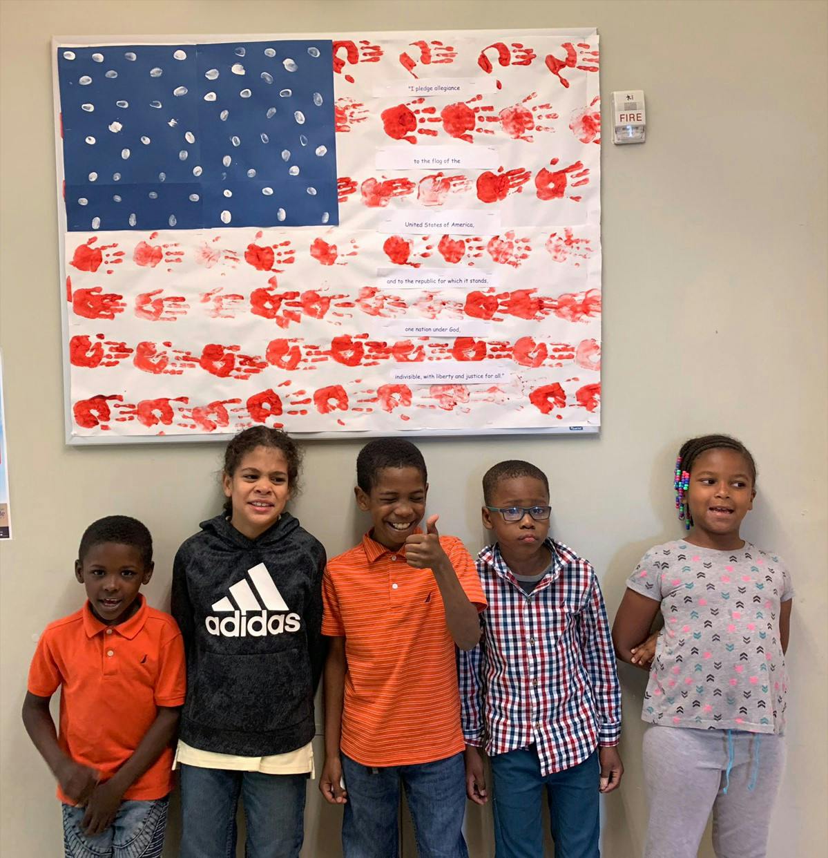Five children standing in front of a flag made of handprints