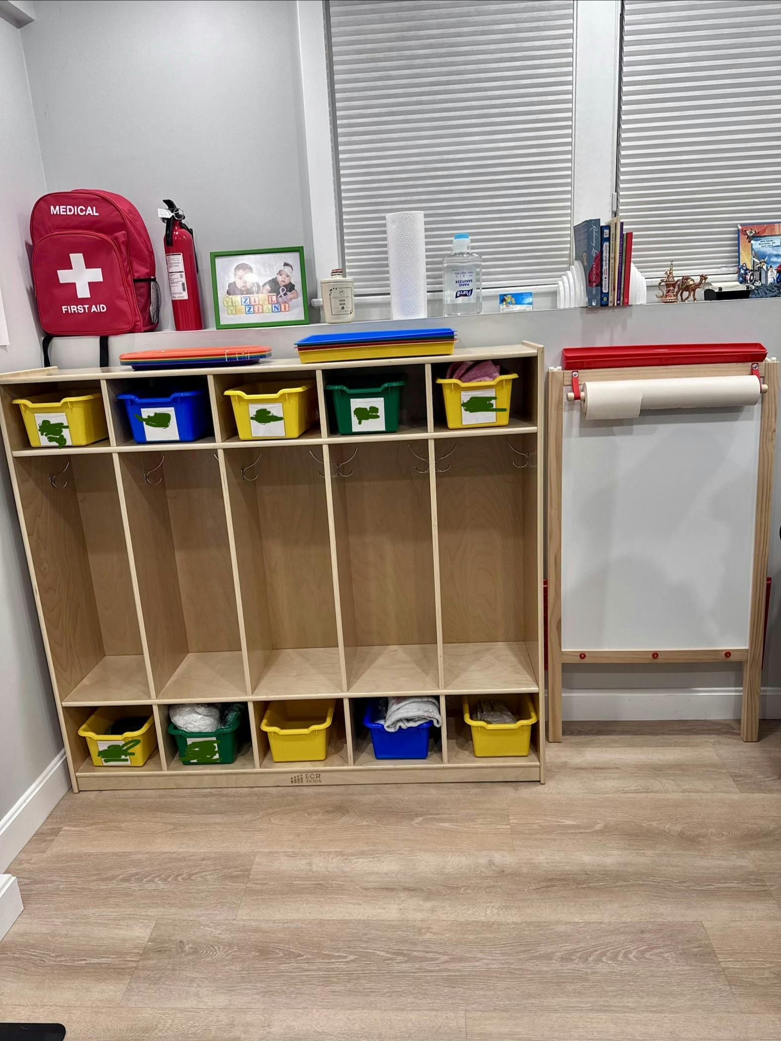 Wooden cubby storage unit with colorful bins and an adjacent easel
