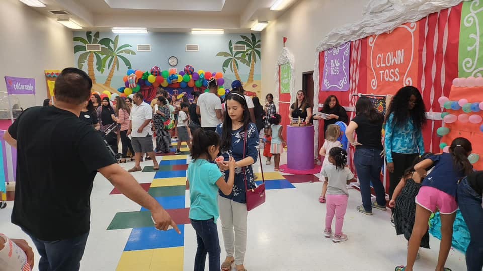 People and children gathered in a large room with balloons and carnival games