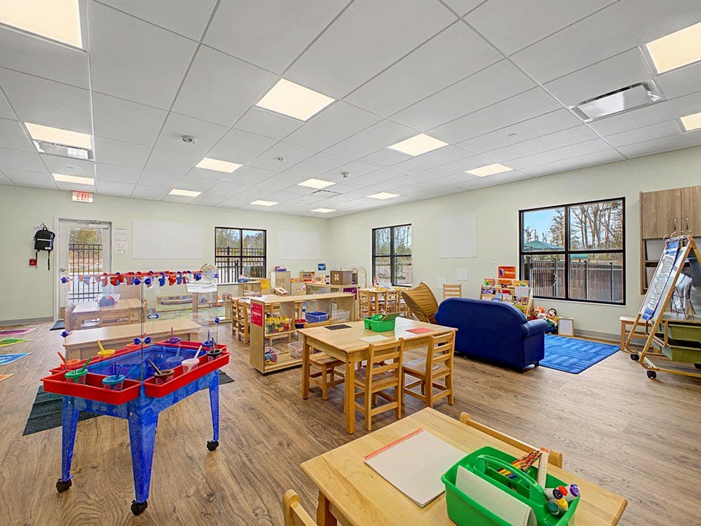A colorful and brightly lit classroom with small tables and a blue sofa