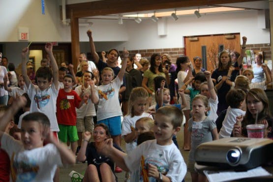 Large group of children and adults with arms raised