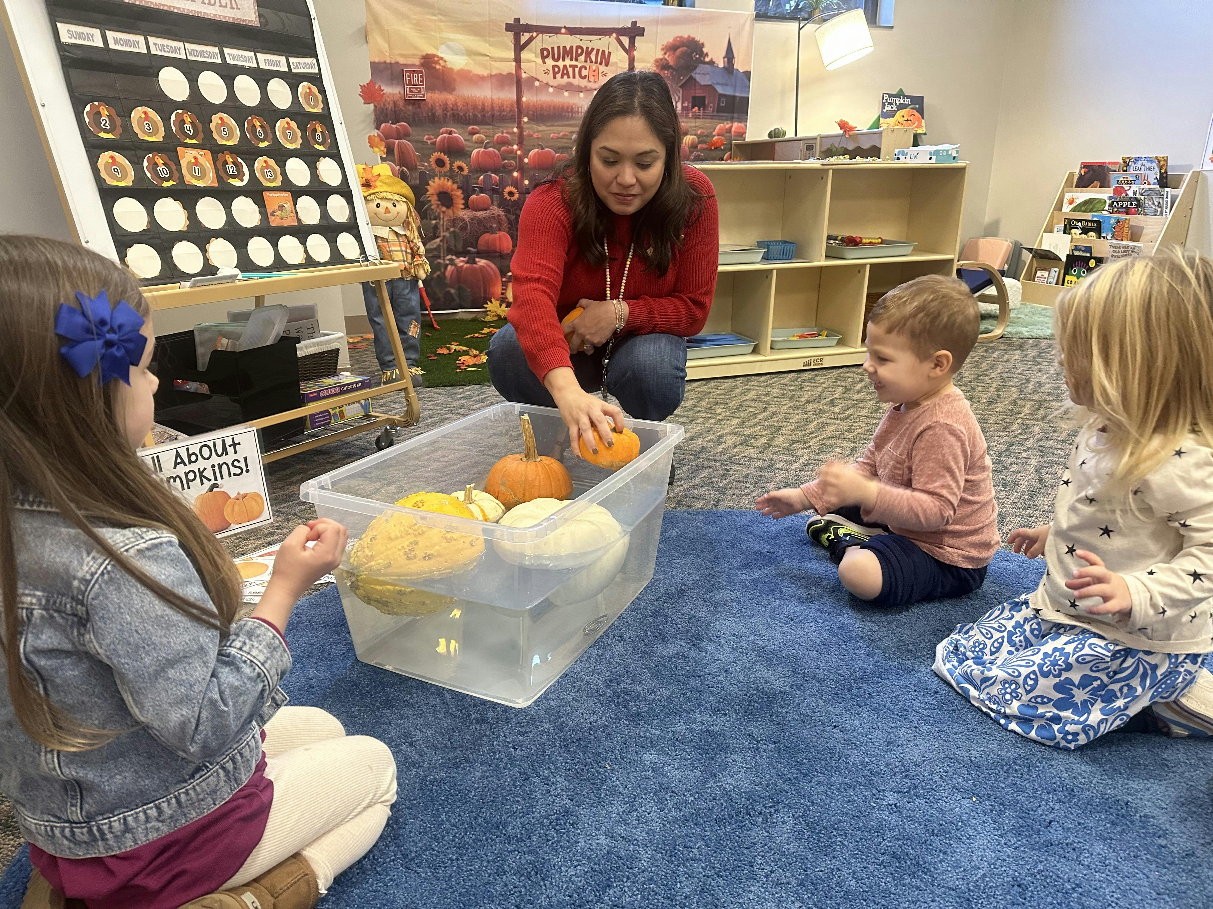 Adult and three children in a classroom playing with pumpkins in a clear bin of water
