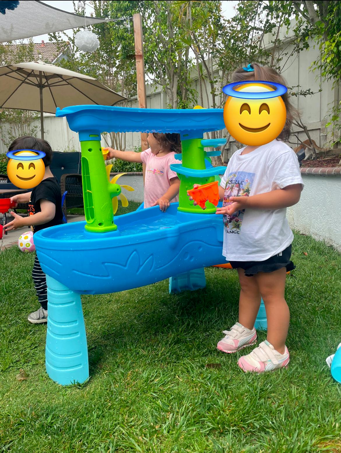 Three children playing with a blue water table outdoors