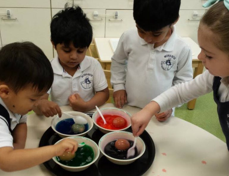 Children dyeing eggs in bowls of colored liquid