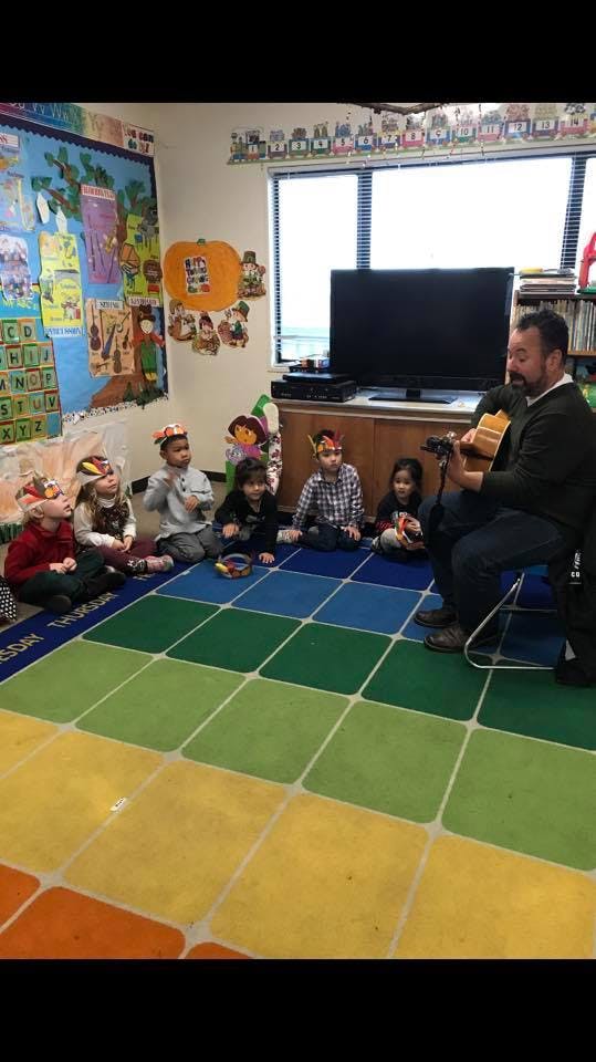 Adult playing guitar for children sitting on a colorful rug in a classroom
