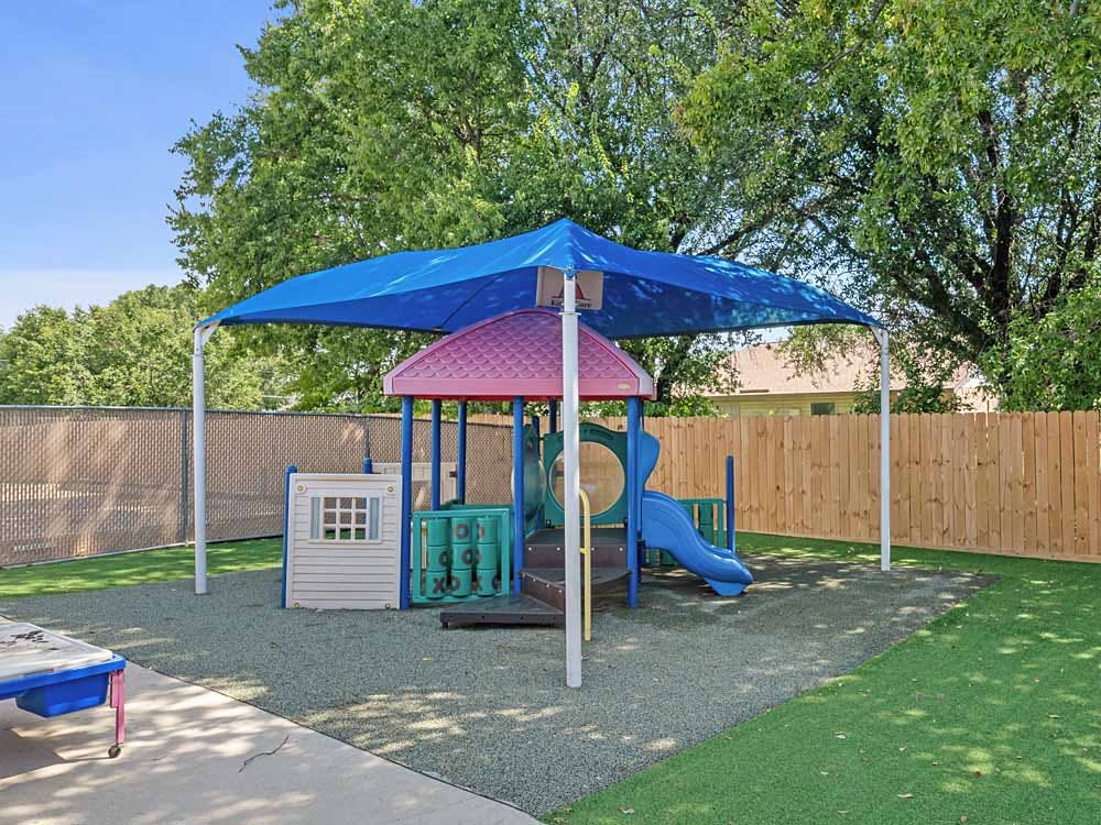 Colorful playground structure with a blue shade covering an artificial turf area