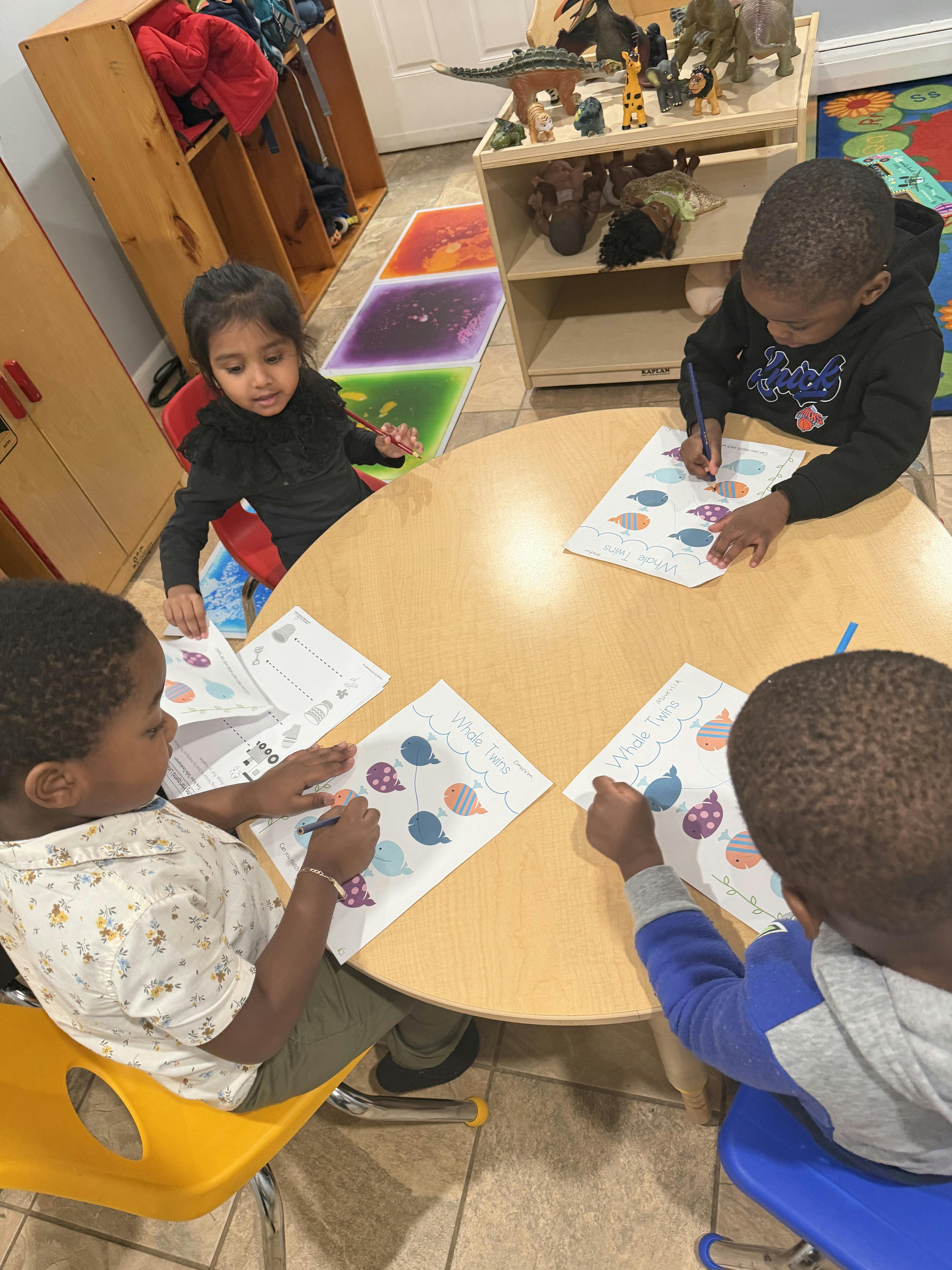Four children sitting at a circular table drawing on worksheets
