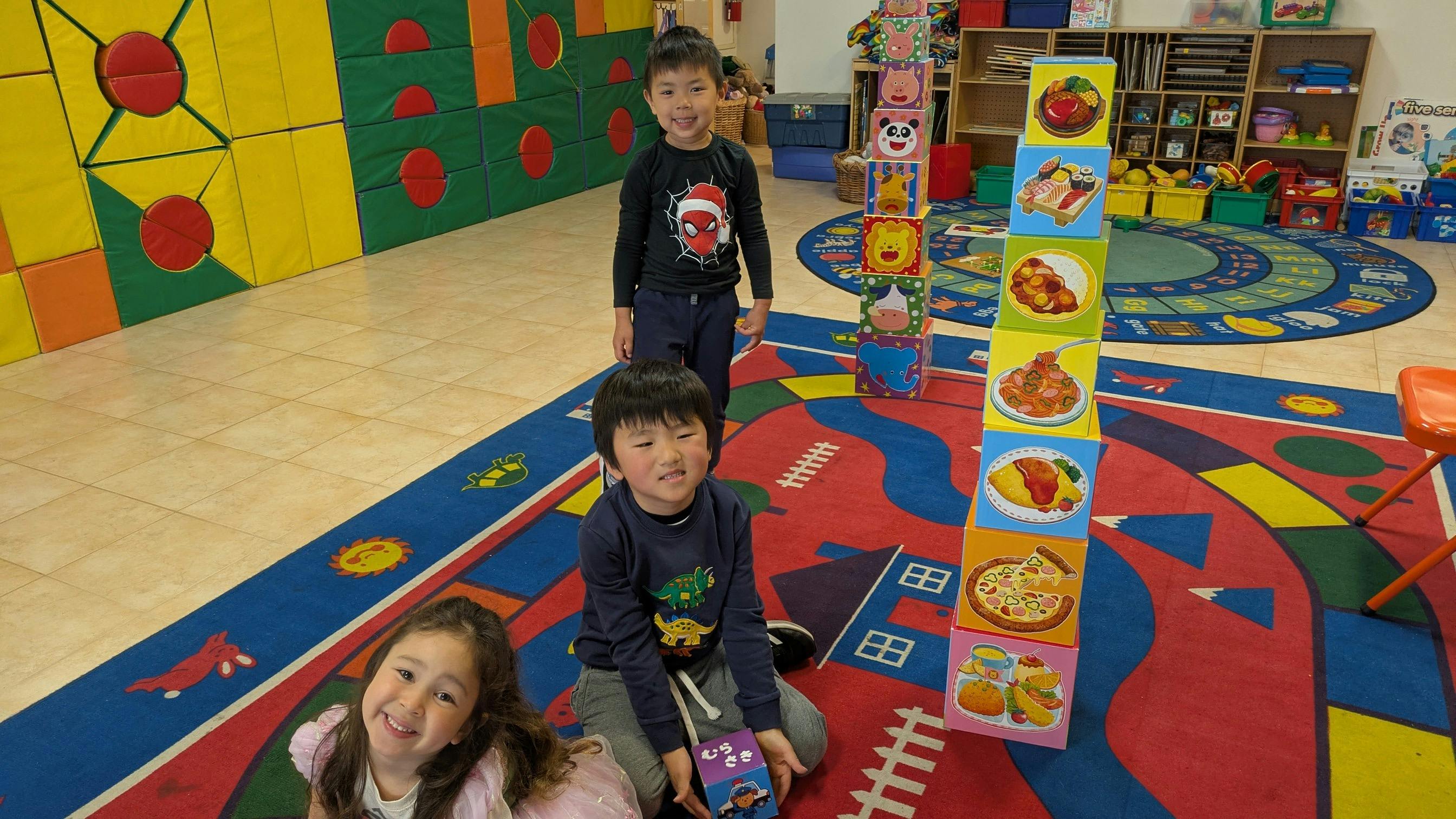 Children playing with a stack of food-themed blocks in a classroom