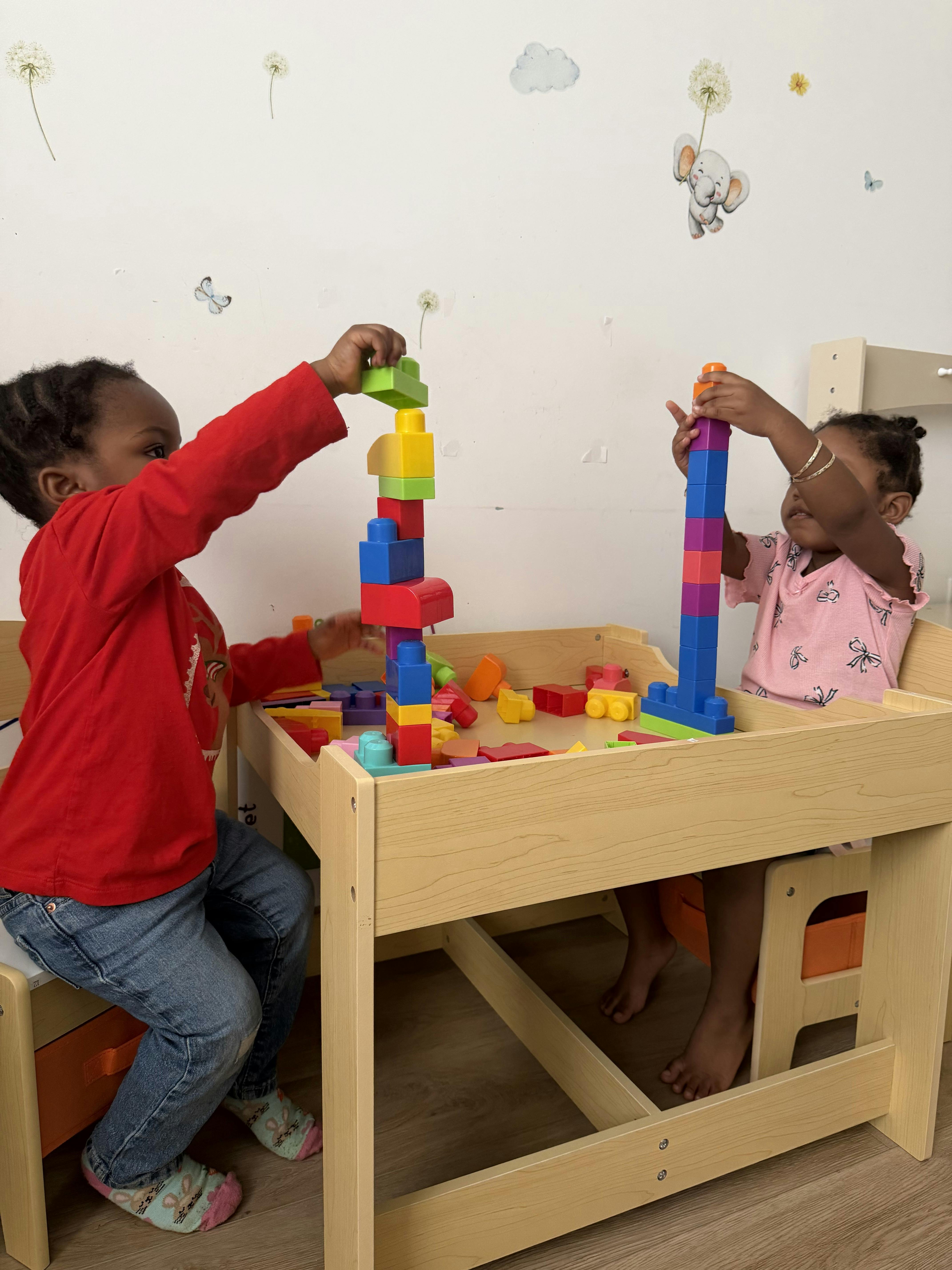 Two children stacking colorful plastic building blocks at a wooden table