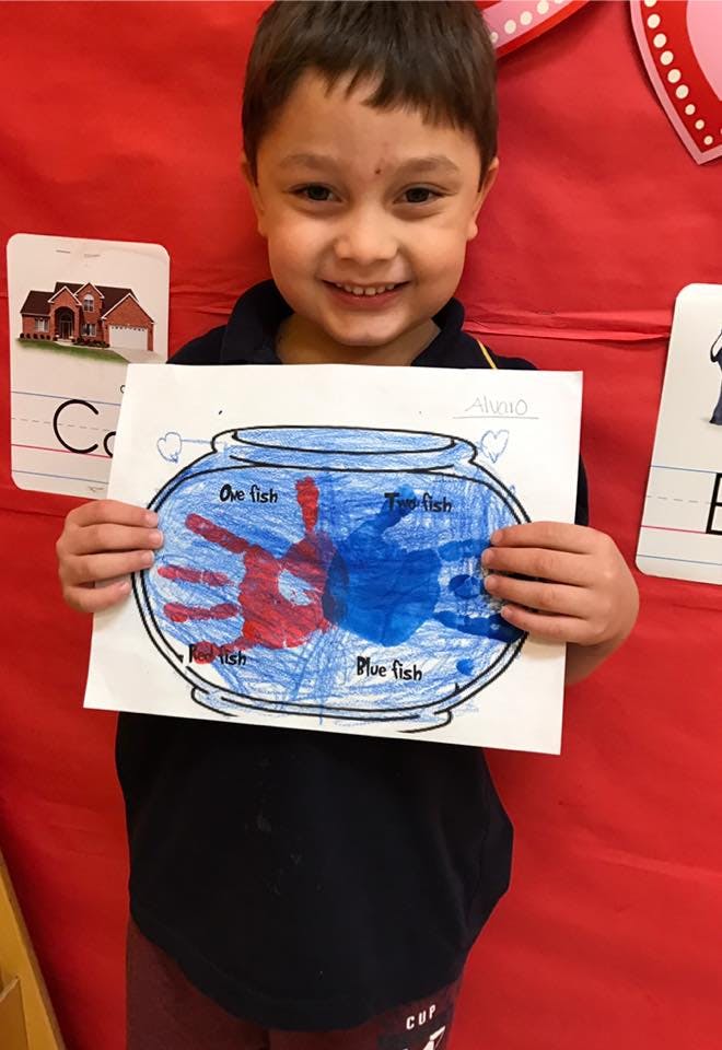 Child holding up a drawing of a fishbowl with red and blue handprints