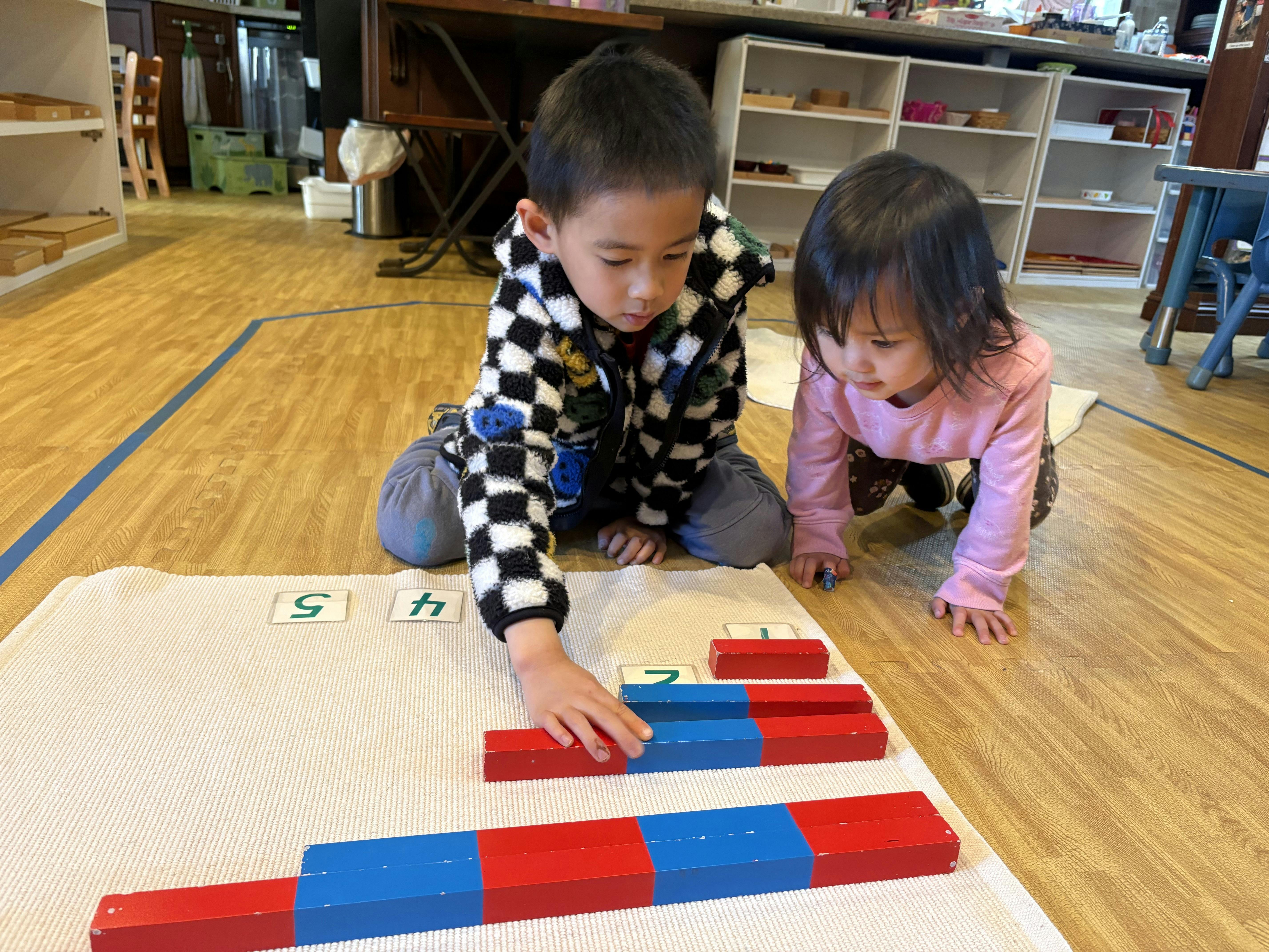Two children on the floor with number cards and red and blue blocks