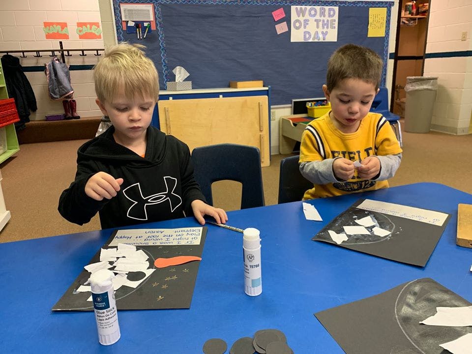 Two children doing crafts at a table in a classroom