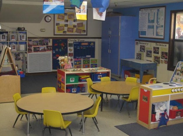 Classroom with child-sized tables and chairs, play kitchen, and storage shelves
