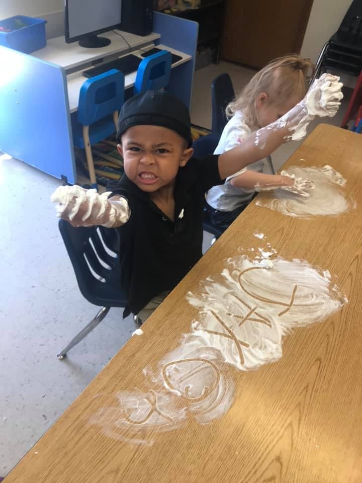 Child with shaving cream on arm and another child with shaving cream on table