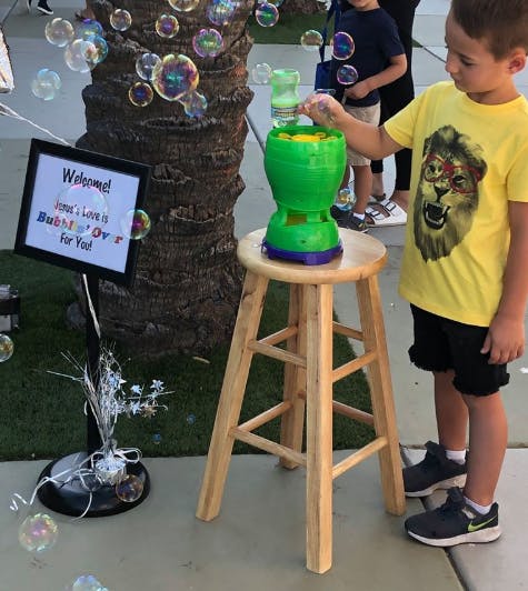 Child operating a bubble machine on a stool with a welcome sign nearby