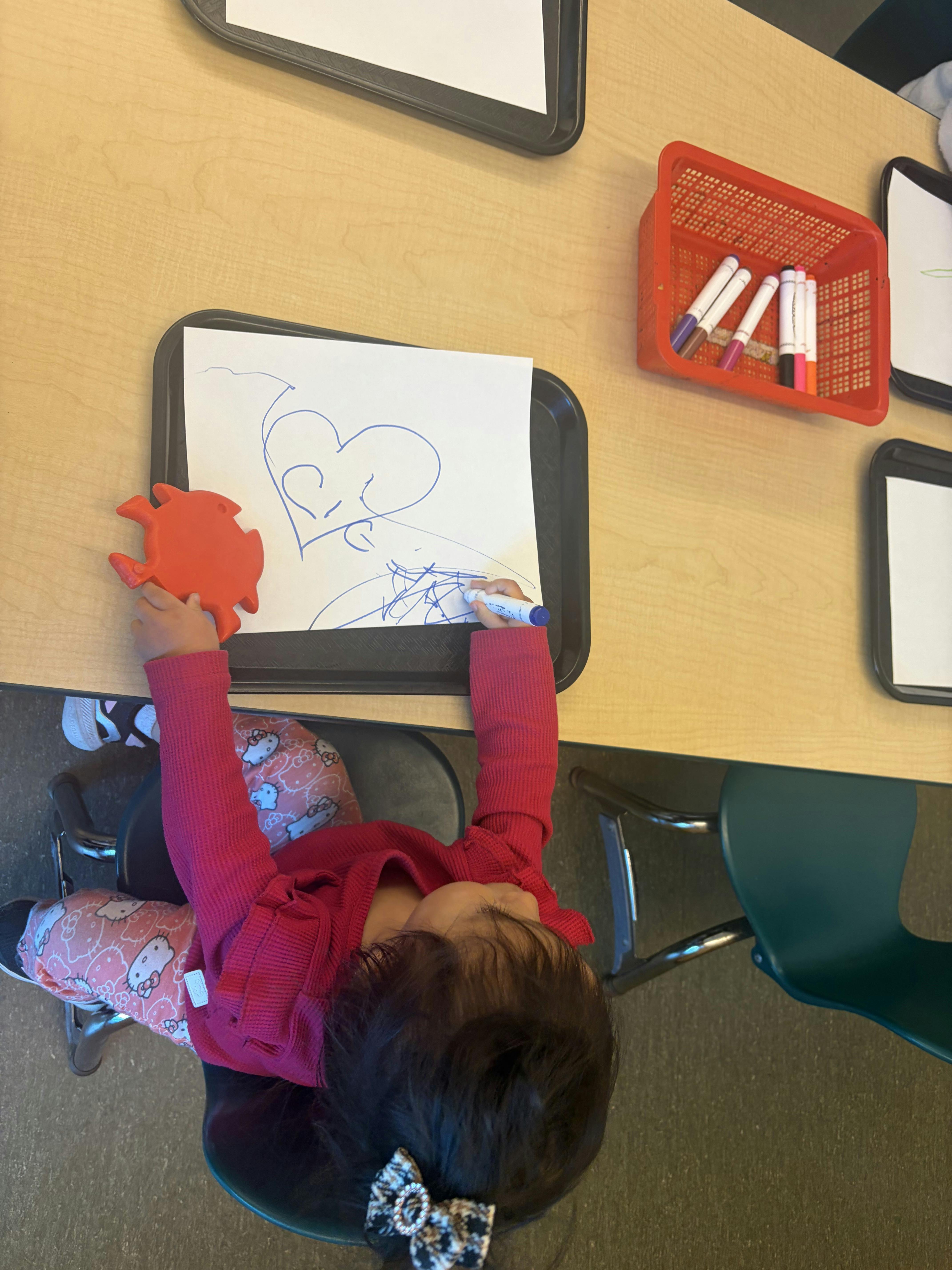 Child drawing on paper with a blue marker at a table