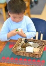 Child playing with small objects from a basket at a table