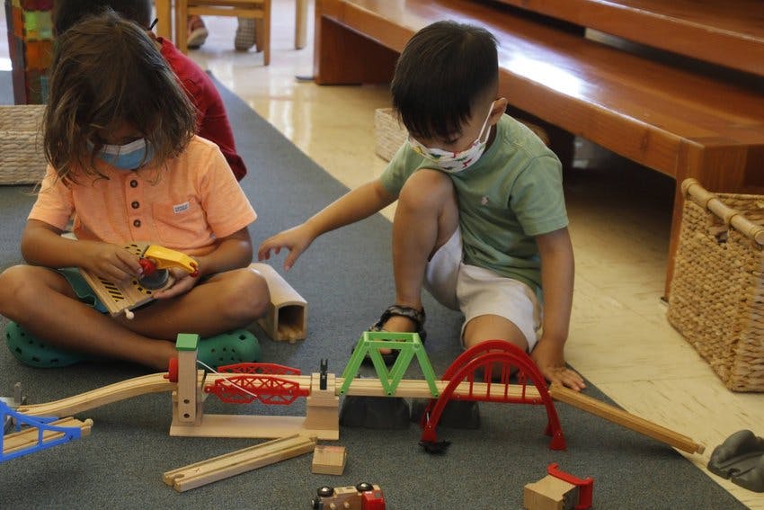 Two children playing with a wooden train set on the floor