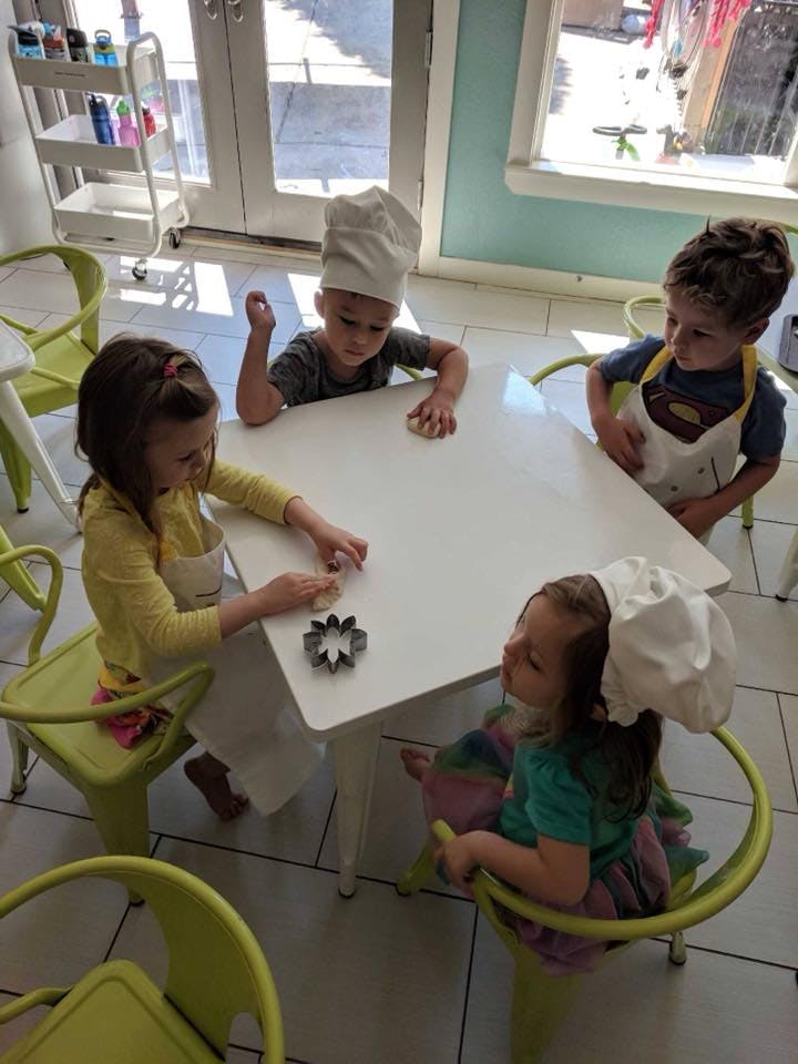 Four children in chef hats and aprons at a table with cookie cutters