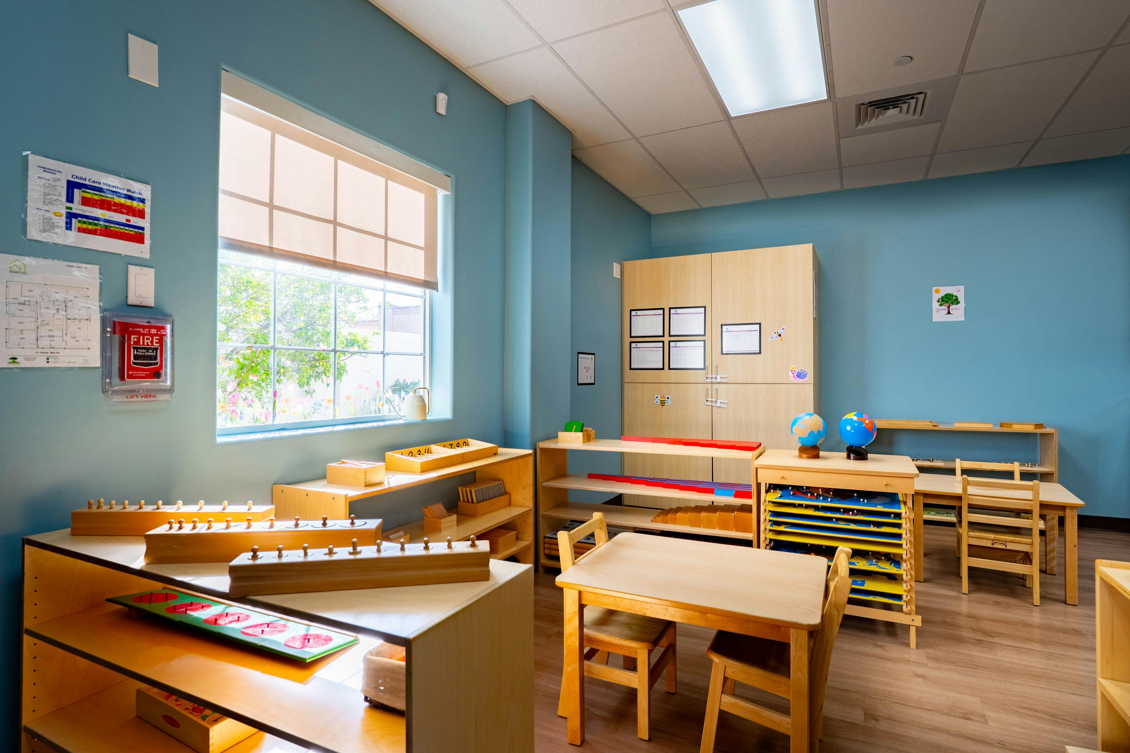 Classroom with child-sized tables and chairs, learning materials on shelves