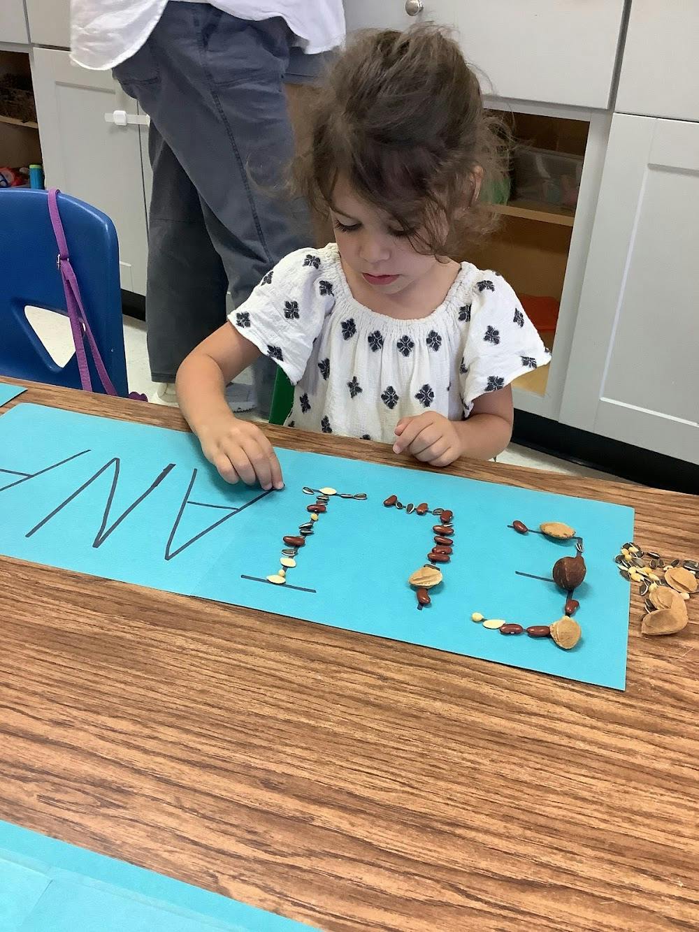 Child placing seeds on paper letters to form a name