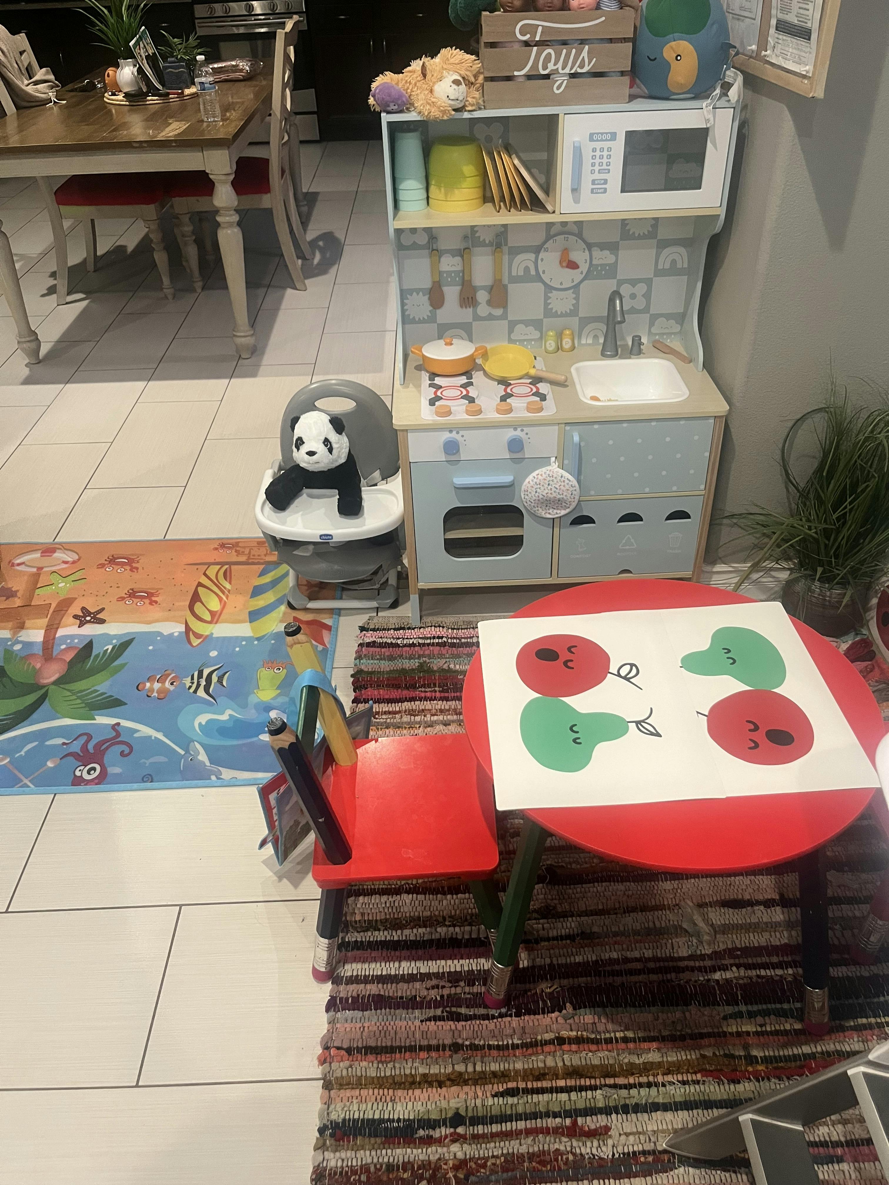 Child's play kitchen with a panda toy in a high chair and a small table with drawing