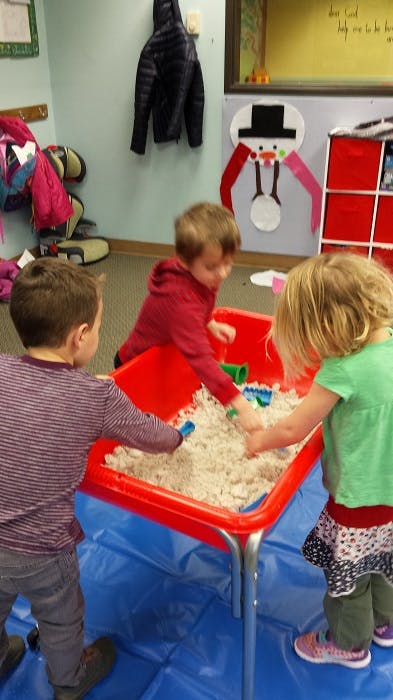 Three children playing in a sand table in a classroom