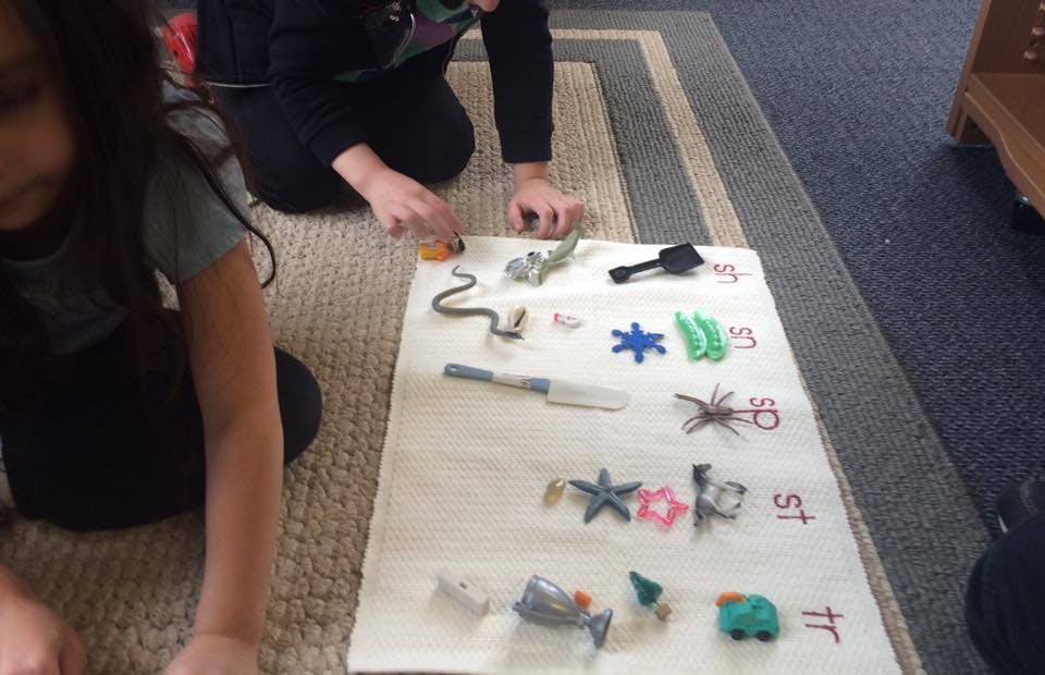Two people sorting small objects on a mat with letters