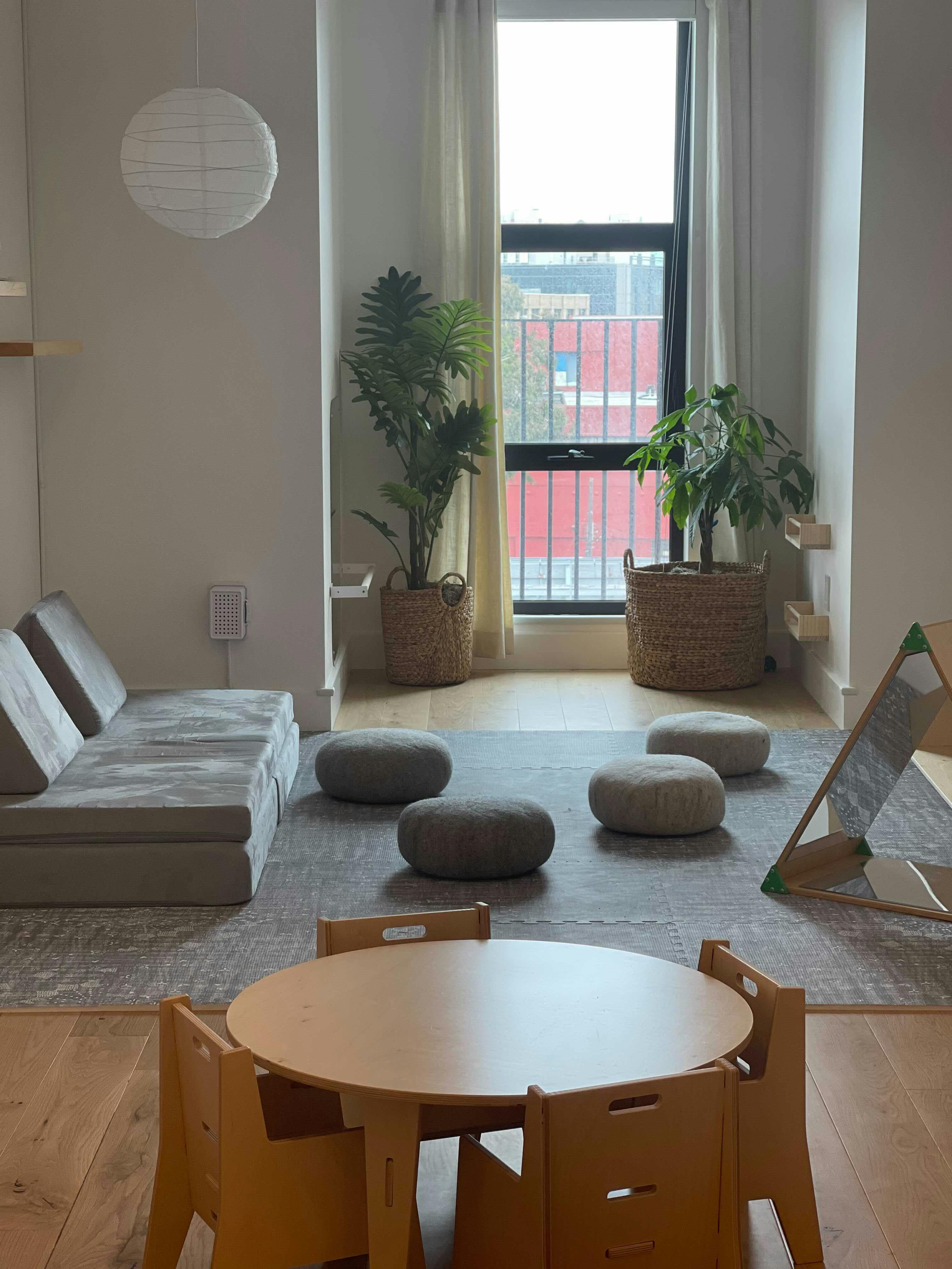 Children's play area with small table and chairs, floor cushions, and plants