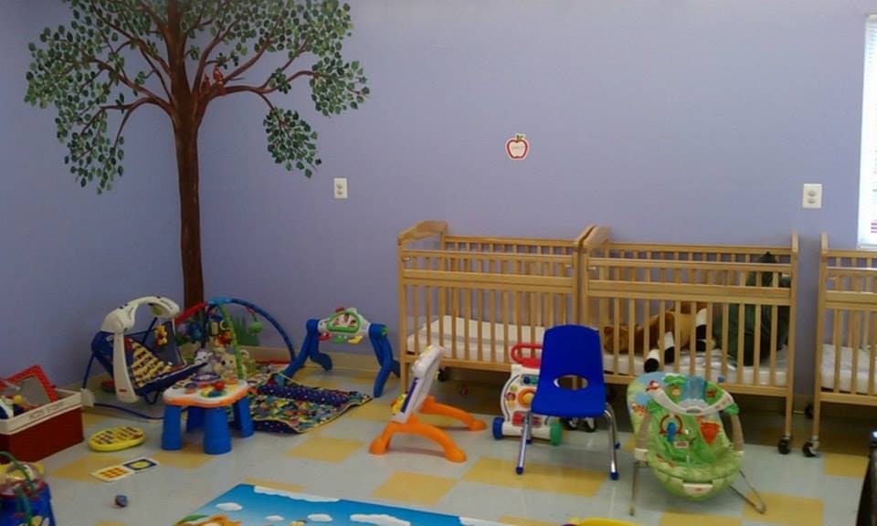 Nursery room with cribs, playmats, and a tree mural on the wall