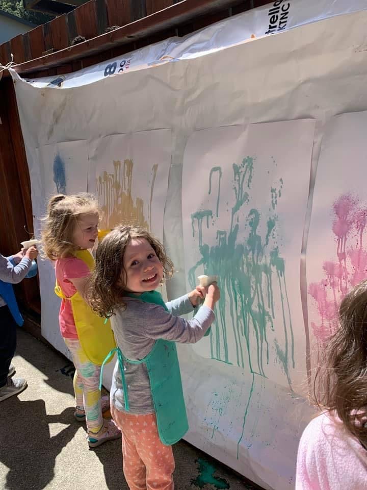Children painting on a large white sheet outdoors