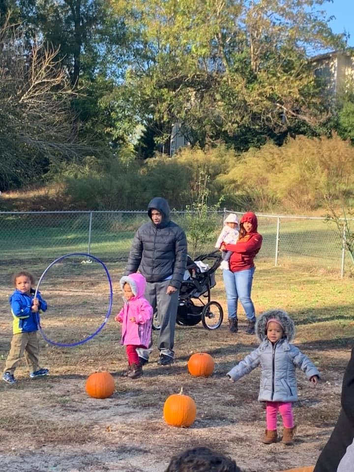 People and children outdoors with pumpkins and a hula hoop