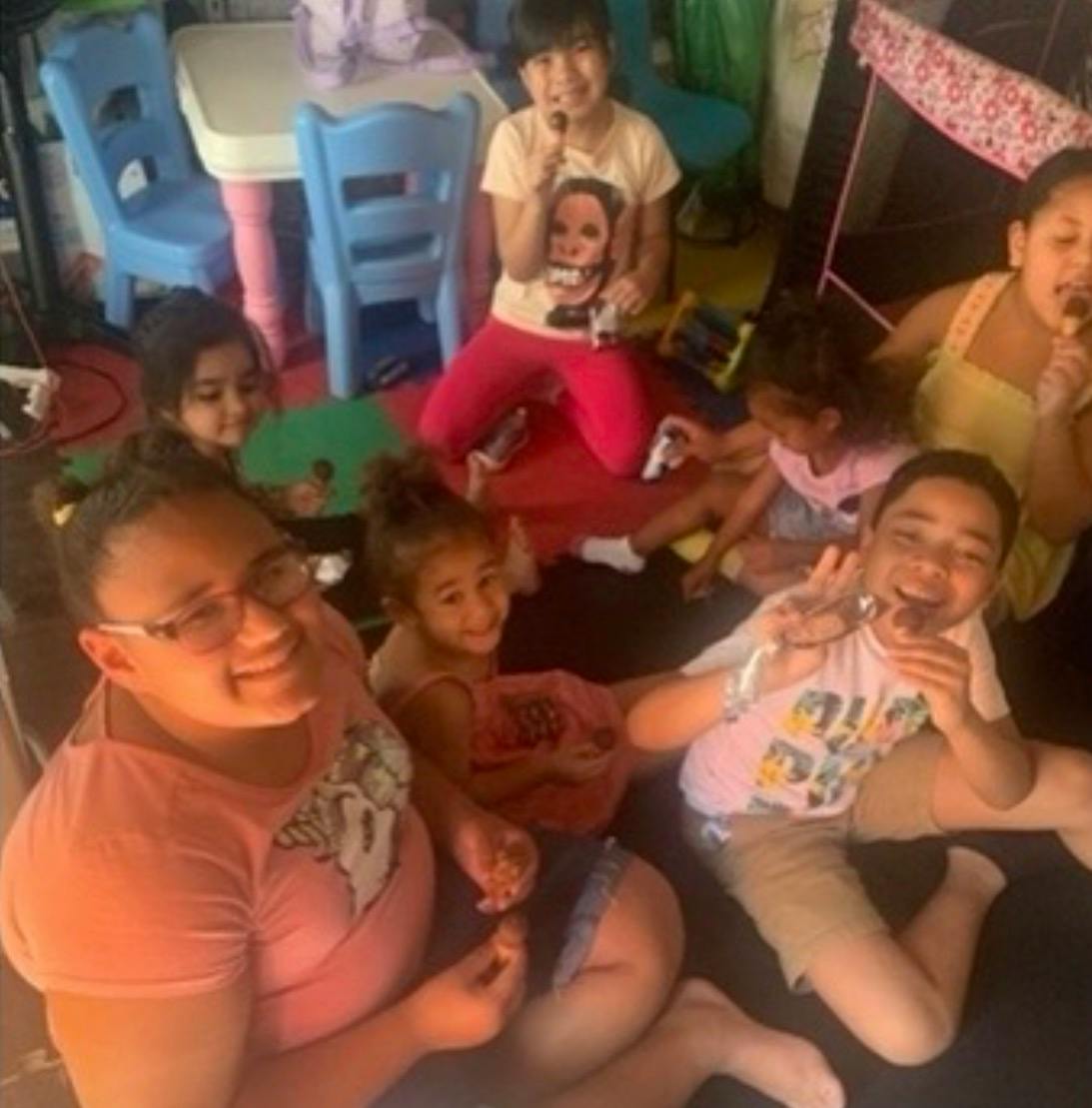Group of children and a person sitting on the floor, some eating popsicles